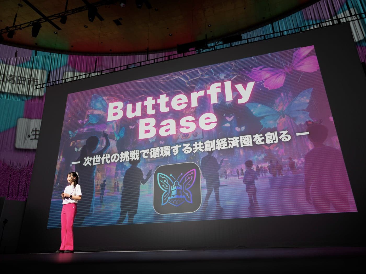 大阪・関西万博のHERO EXPOで登壇する様子。大型スクリーンに『ButterflyBase — 次世代の挑戦で循環する共創経済圏を創る』が映されている